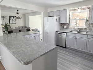 Kitchen with gray cabinets, backsplash, stainless steel dishwasher, light wood-style flooring, and hanging lights