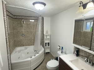 Bathroom with a combined bath / shower with jetted tub, a textured ceiling, vanity, and dark tile patterned flooring