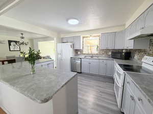 Kitchen with white appliances, gray cabinets, tasteful backsplash, light wood-style flooring, and light countertops