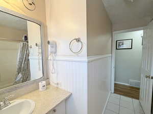 Full bathroom with vanity, a textured ceiling, light tile patterned floors, curtained shower, and a wainscoted wall