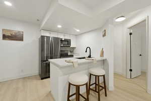 Kitchen with a kitchen bar, stainless steel appliances, a peninsula, white cabinets, and light wood-type flooring