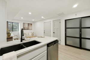 Kitchen with stainless steel dishwasher, light stone countertops, white cabinets, light wood-style flooring, and recessed lighting
