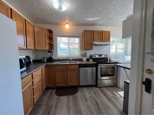 Kitchen with dark countertops, stainless steel appliances, wood finish cabinets, open shelves, and a textured ceiling