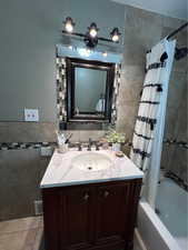 Full bath with tile walls, vanity, and shower / bathtub combination with curtain