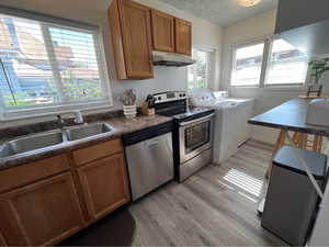 Kitchen featuring stainless steel appliances, dark countertops, a textured ceiling, light wood-style floors, and washer and clothes dryer