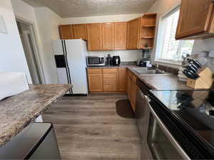 Kitchen featuring open shelves, stainless steel appliances, wood finish cabinetry, dark wood-type flooring, and a textured ceiling