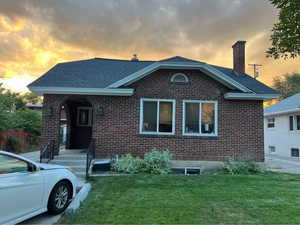 View of front of house featuring a chimney, brick siding, a yard, and a shingled roof