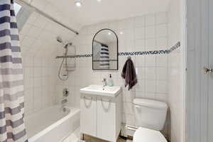 Bathroom featuring vanity, tile walls, a baseboard radiator, shower / bath combination with curtain, and recessed lighting