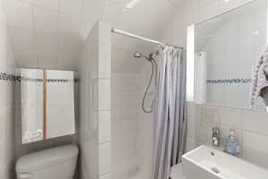Full bathroom featuring tile walls, a stall shower, lofted ceiling, and vanity