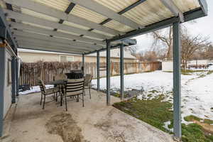 Snow covered patio with outdoor dining space, a patio area, a fenced backyard, and a storage shed