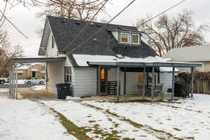 Snow covered back of property featuring roof with shingles, outdoor dining space, and an attached carport