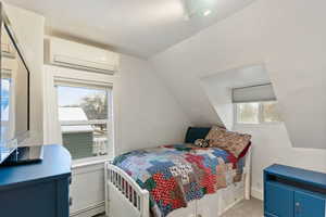 Carpeted bedroom featuring lofted ceiling, a mini split for heating / cooling, and a baseboard heating unit