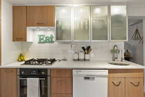 Kitchen featuring stainless steel appliances, glass insert cabinets, light stone countertops, tasteful backsplash, and wood finish cabinets