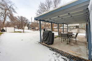 Snow covered patio with a patio, outdoor dining area, area for grilling, and a fenced backyard