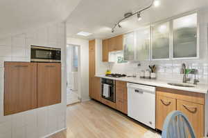 Kitchen featuring glass fronted cabinets, stainless steel appliances, light wood-style floors, light stone countertops, and backsplash