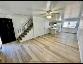 Unfurnished living room featuring light wood-style flooring, a ceiling fan, a textured ceiling, and a baseboard radiator