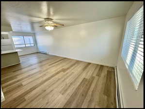 Unfurnished living room featuring light wood-type flooring, baseboard heating, ceiling fan, and a textured ceiling