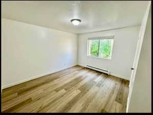 Empty room featuring baseboard heating, light wood-style floors, and a textured ceiling