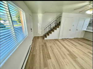 Unfurnished living room with a baseboard radiator, ceiling fan, and light wood finished floors