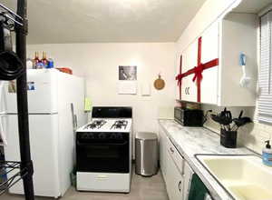 Kitchen with white appliances, light countertops, white cabinetry, light wood-style flooring, and backsplash