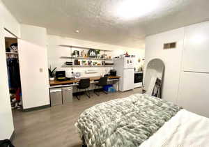 Bedroom featuring built in study area, freestanding refrigerator, light wood-style floors, a closet, and a textured ceiling
