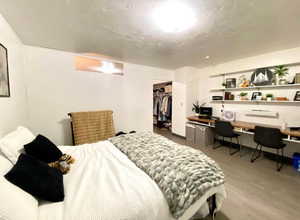 Bedroom with light wood-type flooring, built in study area, a walk in closet, and a textured ceiling
