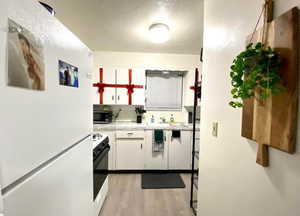 Kitchen with white appliances, light countertops, backsplash, light wood-style flooring, and white cabinets