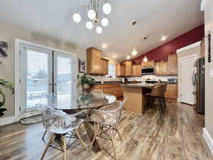 Dining room with light wood finished floors, lofted ceiling, french doors, and hanging lights