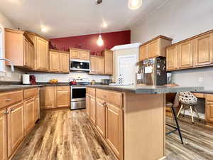 Kitchen featuring dark countertops, lofted ceiling, stainless steel appliances, a breakfast bar area, and a kitchen island