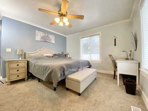 Bedroom with light colored carpet, ornamental molding, and ceiling fan