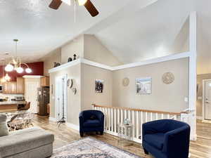 Living area with a chandelier, light wood-style floors, lofted ceiling, and a ceiling fan