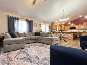 Living area featuring light wood-style flooring, ceiling fan, lofted ceiling, and suspended lighting