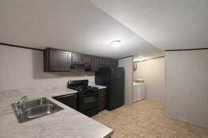 Kitchen with black appliances, light countertops, a textured ceiling, washer and clothes dryer, and dark wood finish cabinetry