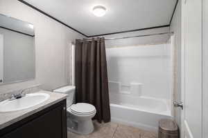 Full bathroom featuring vanity, shower / tub combo with curtain, a textured ceiling, light tile patterned flooring, and ornamental molding