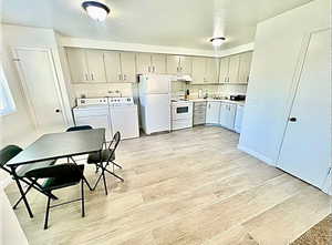 Kitchen featuring light countertops, white appliances, wood tiled floors, washing machine and dryer, and gray cabinets