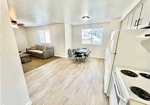 Kitchen with white appliances, light wood finished floors, a textured ceiling, ceiling fan, and light countertops