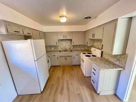 Kitchen featuring white appliances, light wood finished floors, light countertops, decorative backsplash, and gray cabinets