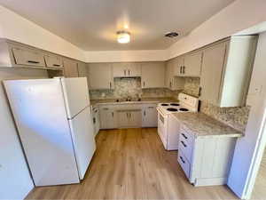 Kitchen featuring white appliances, light wood finished floors, light countertops, decorative backsplash, and gray cabinets