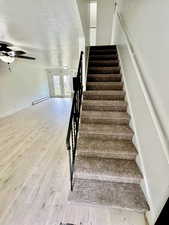 Staircase featuring a textured ceiling, french doors, a baseboard heating unit, wood finished floors, and a ceiling fan