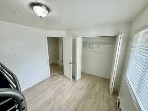 Unfurnished bedroom with light wood-style flooring, a baseboard heating unit, a closet, and a textured ceiling