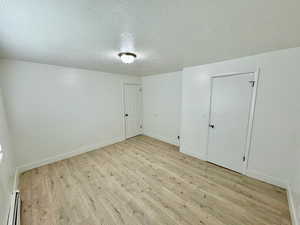 Unfurnished room with a textured ceiling, light wood-style floors, and baseboard heating