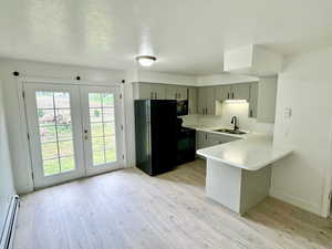 Kitchen featuring light countertops, a peninsula, a textured ceiling, black appliances, and a baseboard heating unit
