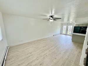 Unfurnished living room featuring baseboard heating, a textured ceiling, light wood-style floors, and french doors