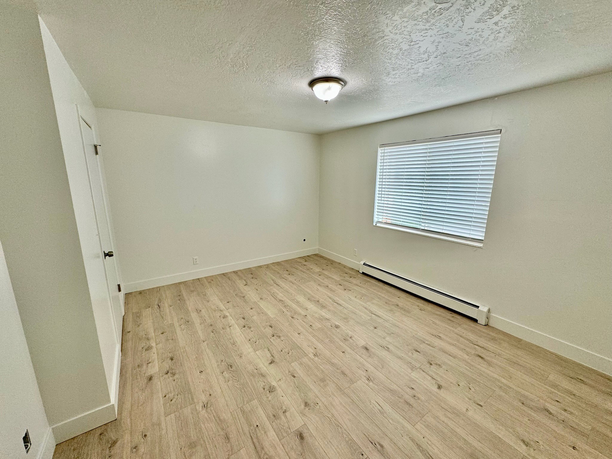 Unfurnished room featuring a baseboard heating unit, light wood-style floors, and a textured ceiling