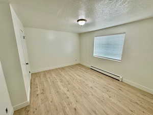 Unfurnished room featuring a baseboard heating unit, light wood-style floors, and a textured ceiling