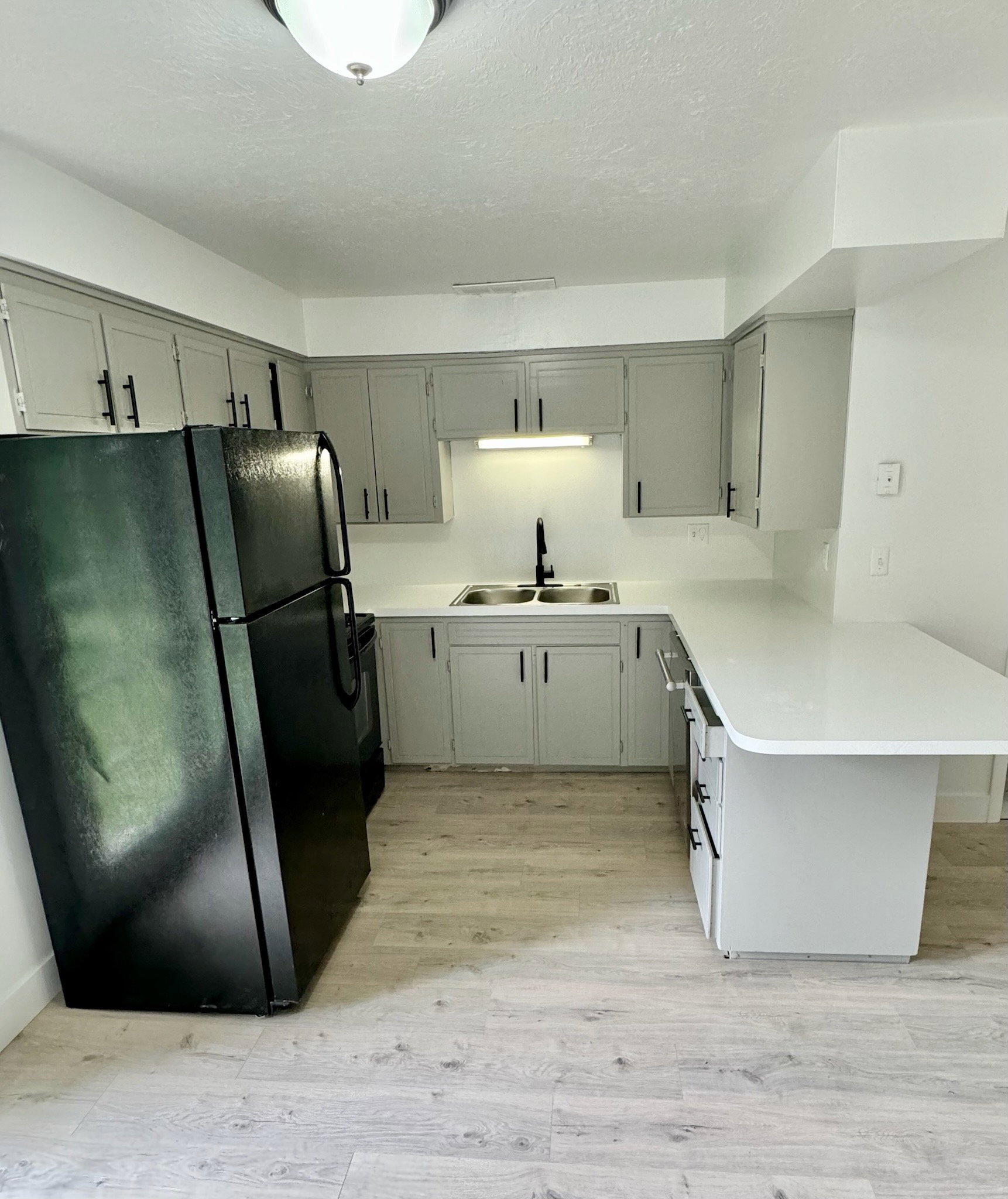 Kitchen with black appliances, light countertops, light wood-type flooring, a peninsula, and a textured ceiling