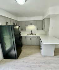 Kitchen with black appliances, light countertops, light wood-type flooring, a peninsula, and a textured ceiling
