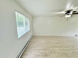 Unfurnished room featuring a baseboard heating unit, a ceiling fan, light wood-style floors, and a textured ceiling