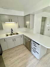 Kitchen featuring a peninsula, light countertops, dishwasher, light wood finished floors, and gray cabinets