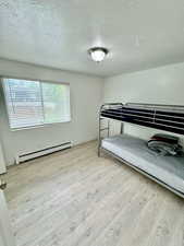 Bedroom with a baseboard radiator, a textured ceiling, and light wood-style floors